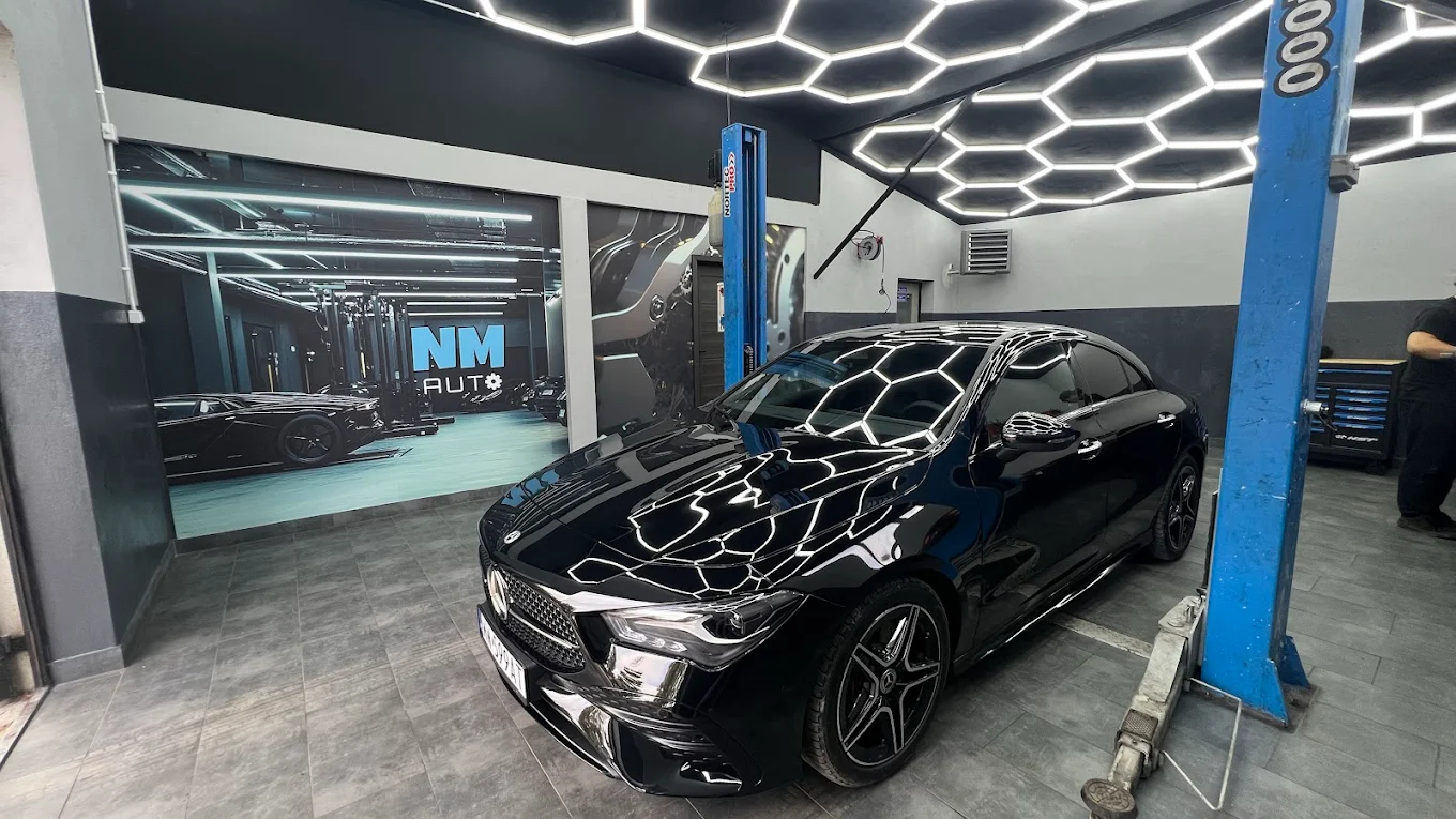 Czarny Mercedes na podnośniku w nowoczesnym warsztacie z oświetleniem w kształcie plastra miodu.