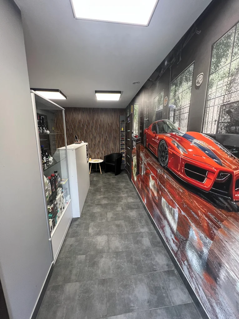 Korytarz poczekalni warsztatu z fototapetą sportowego auta i szklaną gablotą z produktami.