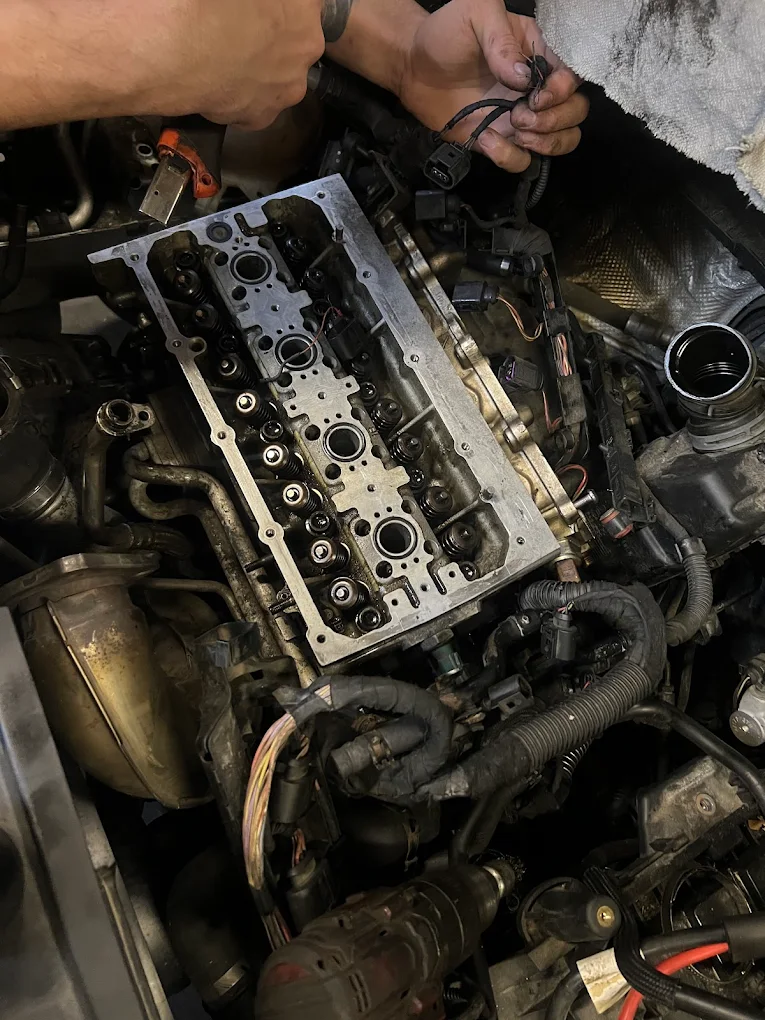 Zbliżenie na otwarty silnik samochodu w trakcie naprawy, widoczne elementy głowicy i okablowania.