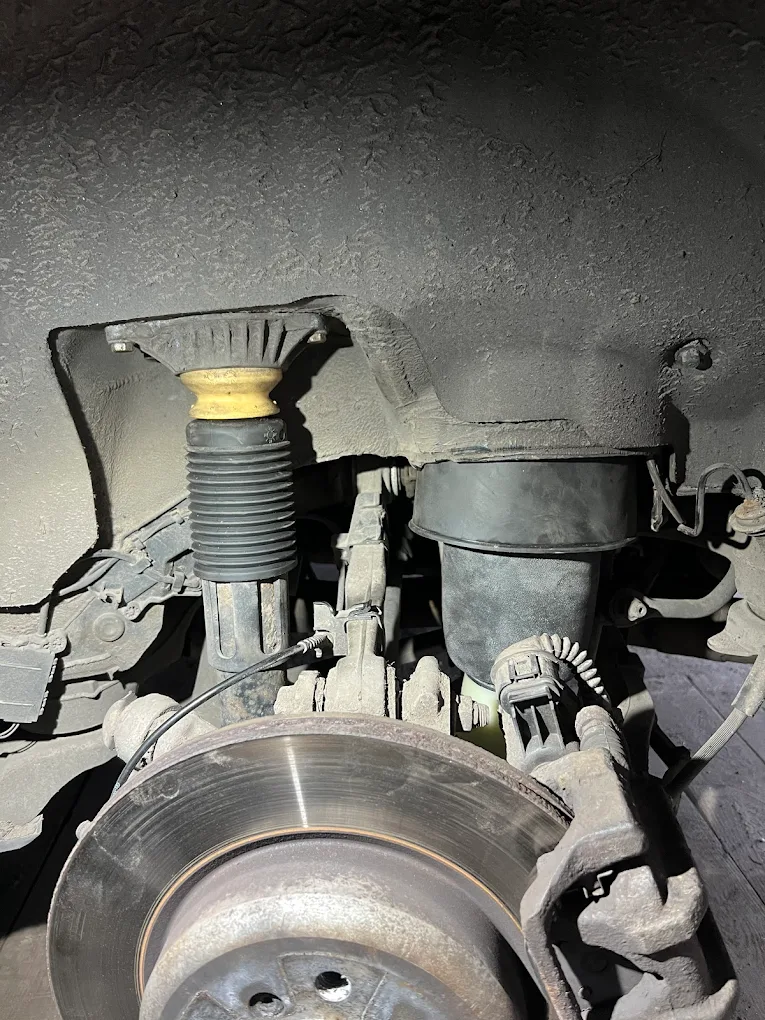 Zużyte zawieszenie i układ hamulcowy samochodu widoczne od spodu podczas kontroli.